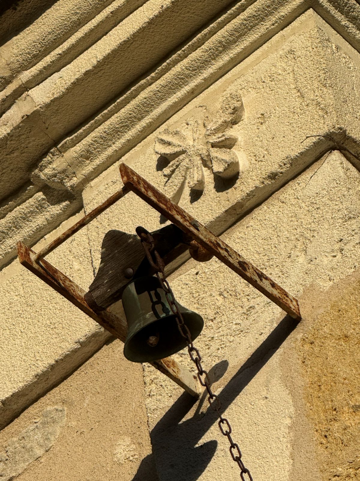 Old bell and chain beneath a carved stone emblem on the house