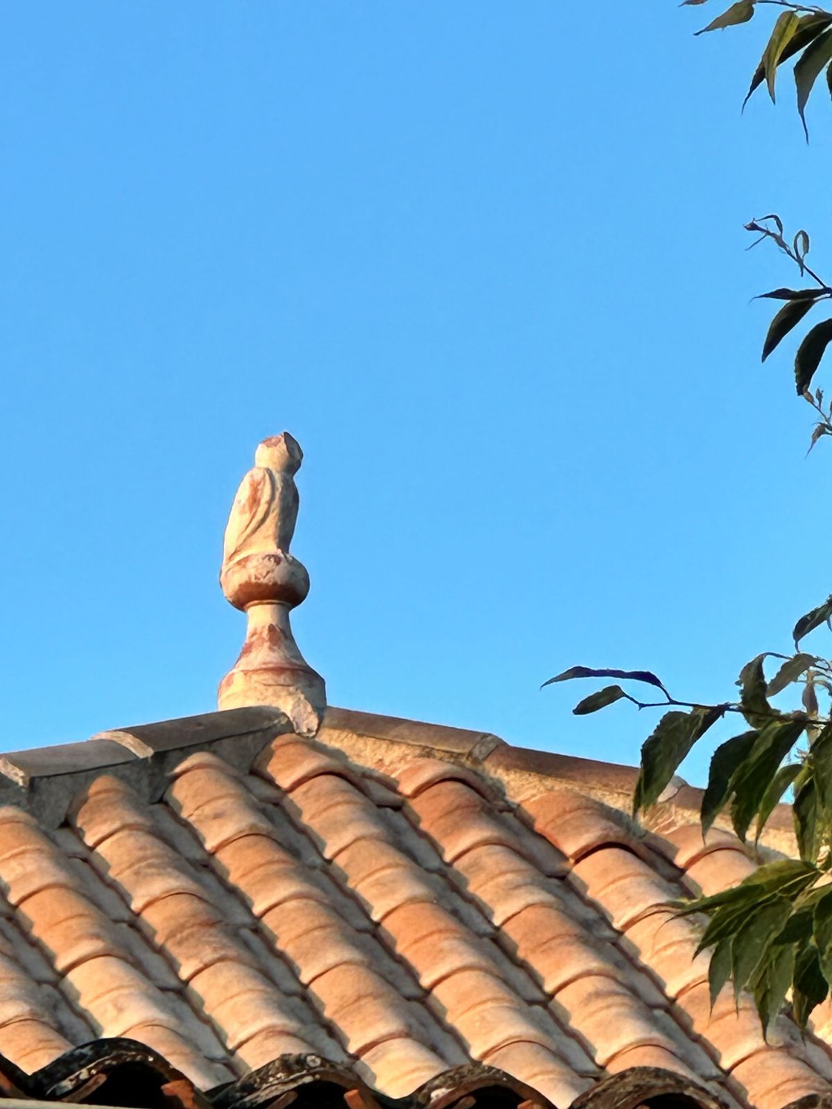 Owl-shaped finial above the terracotta roof tiles against a blue sky