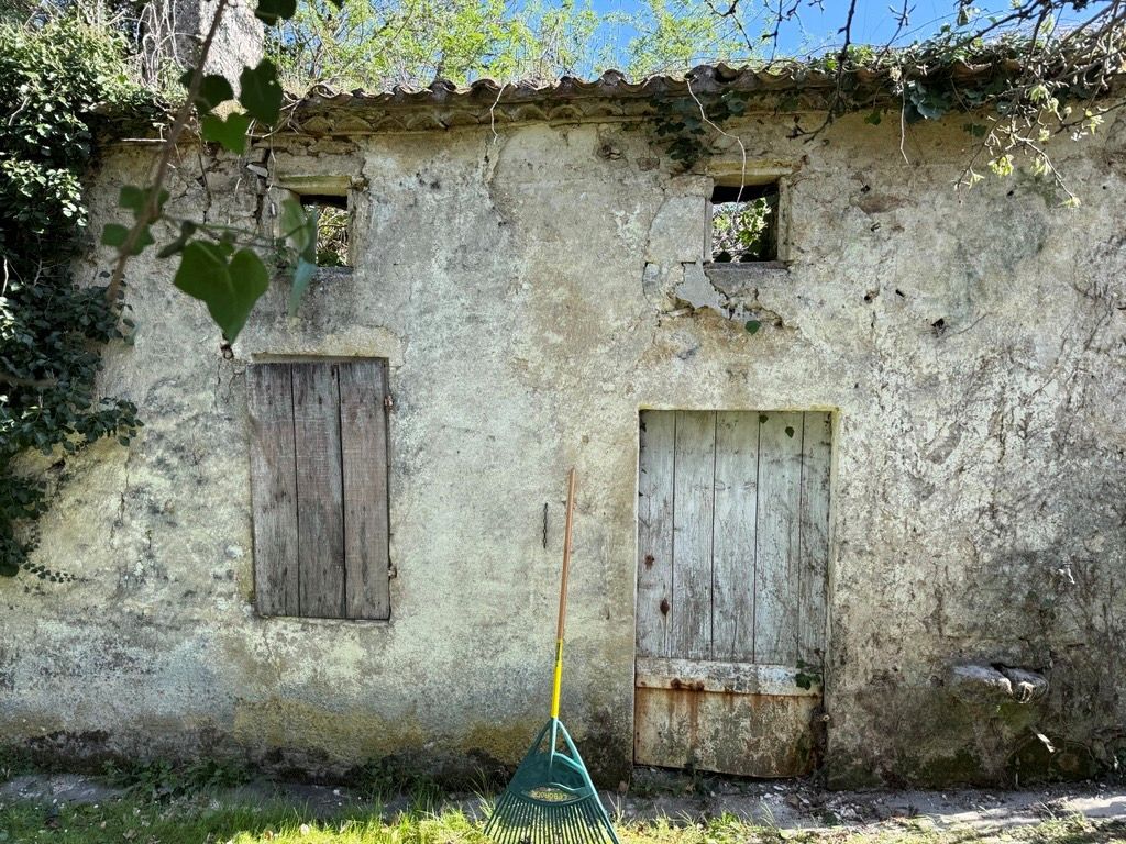 Weathered stone outbuilding with wooden doors and surrounding greenery